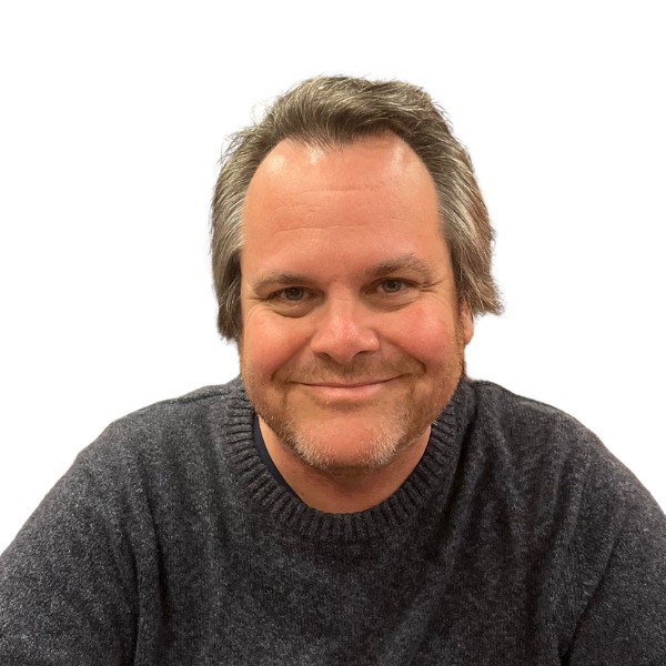 A white man smiles, wearing a blue sweater.